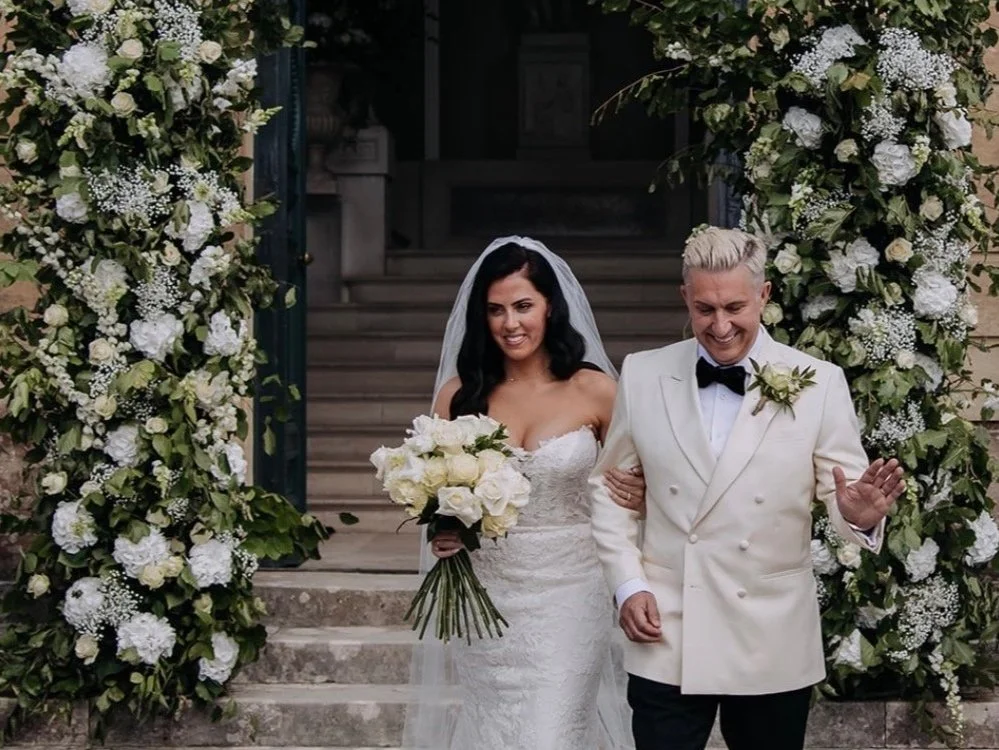 Bride and groom beside a white floral staircase installation