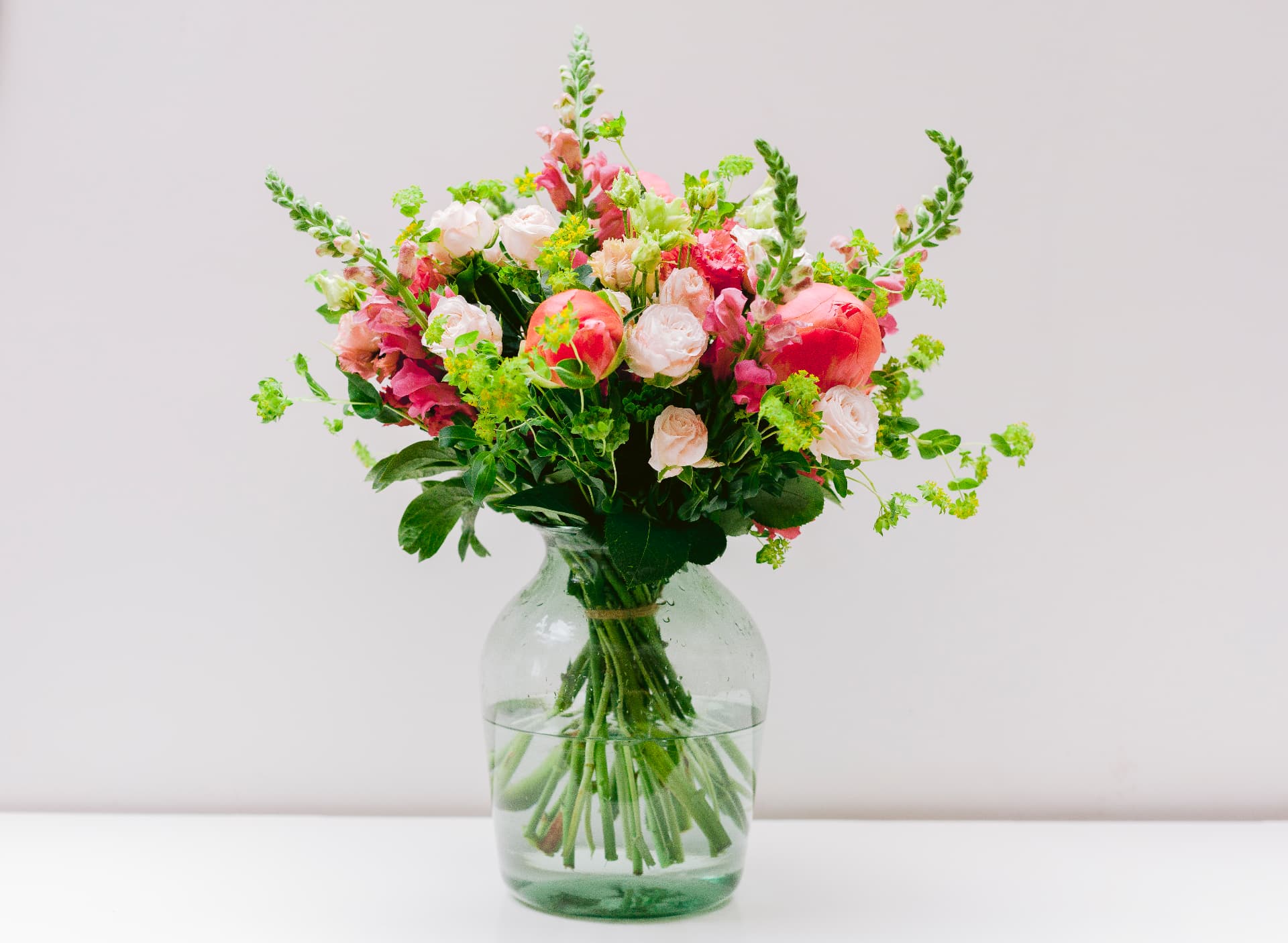 Coral and blush seasonal bouquet with peonies, roses and snapdragons in a glass vase